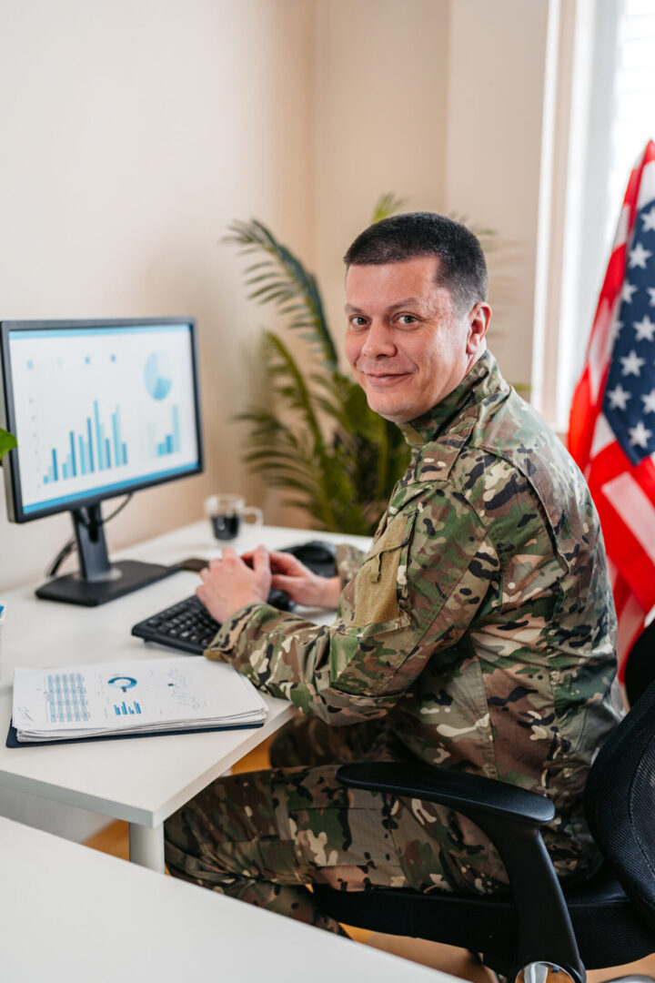 Man in military uniform sitting at a desk in front of an American flag