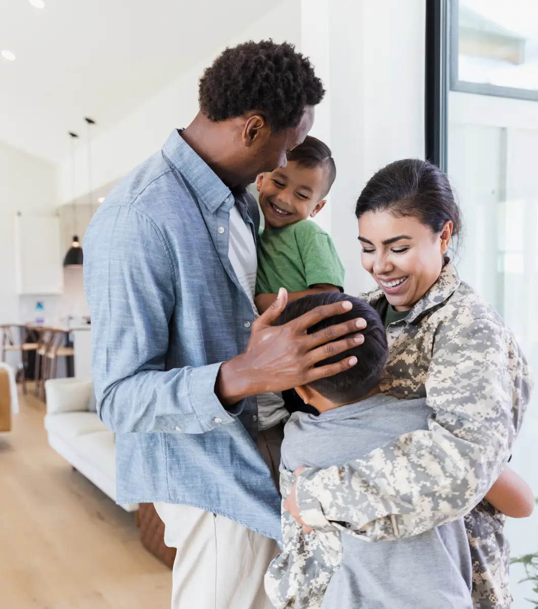 Military family of four, a man, woman and two children, embracing in a living room