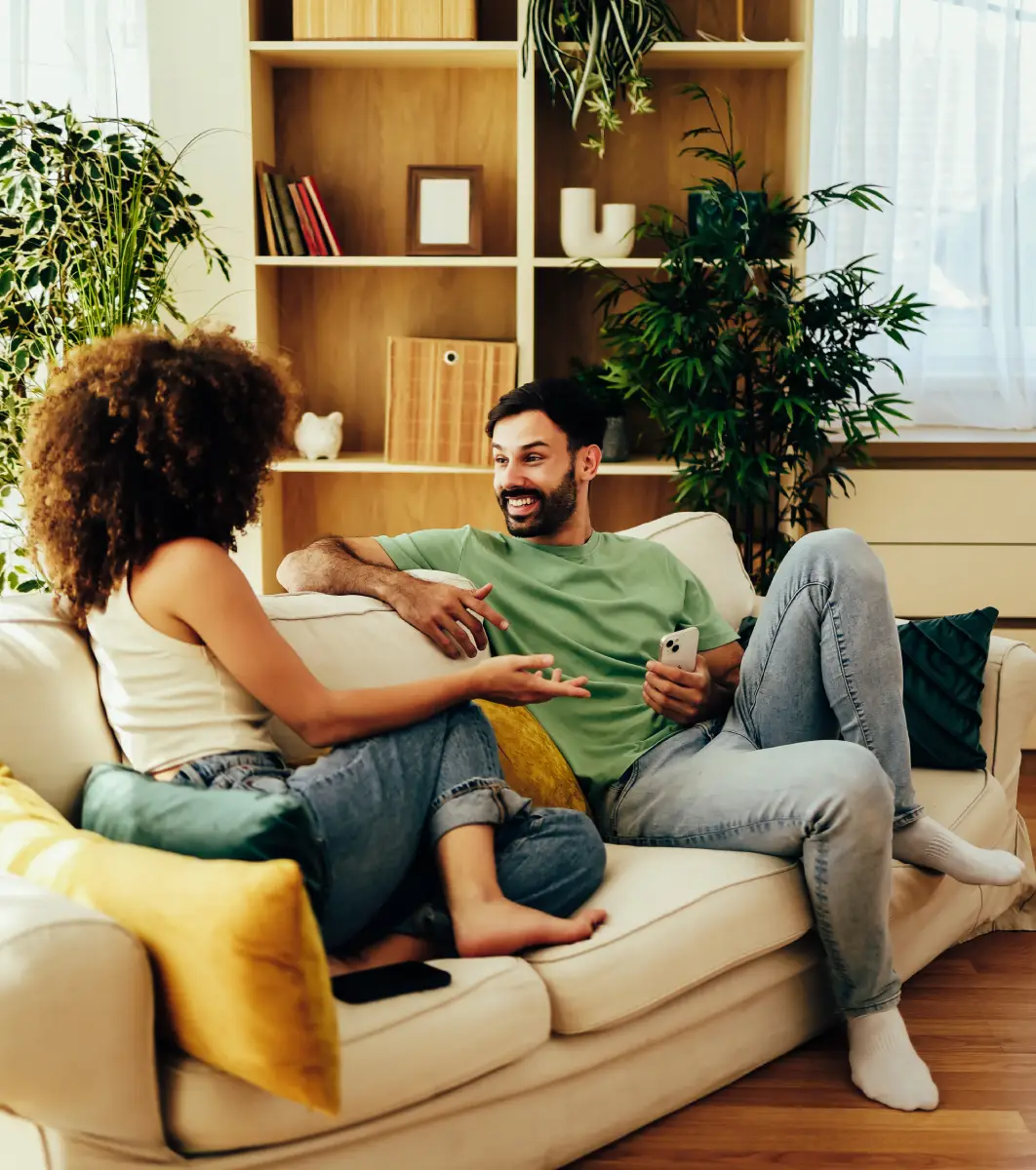 Man and woman sitting on a couch, surrounded by cushions and a mobile phone